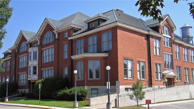 Red brick building with grass and bushes out front. Picture taken from the corner.